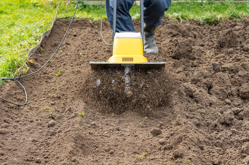 Loosening the soil in the garden beds with an electric hand-held cultivator