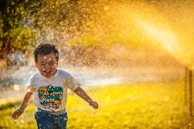Child running around in a water sprinkler.