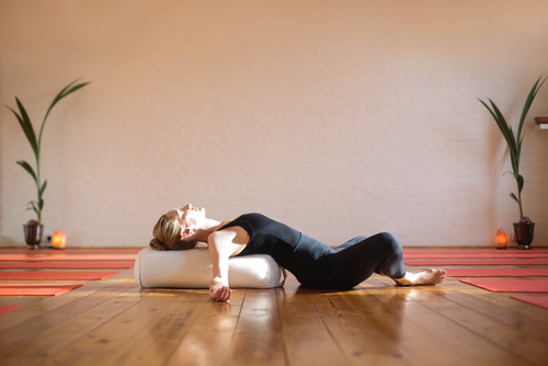 A woman laying in butterfly pose using a bolster. 