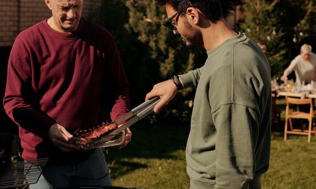 Two men, one handing barbequed meat to the other