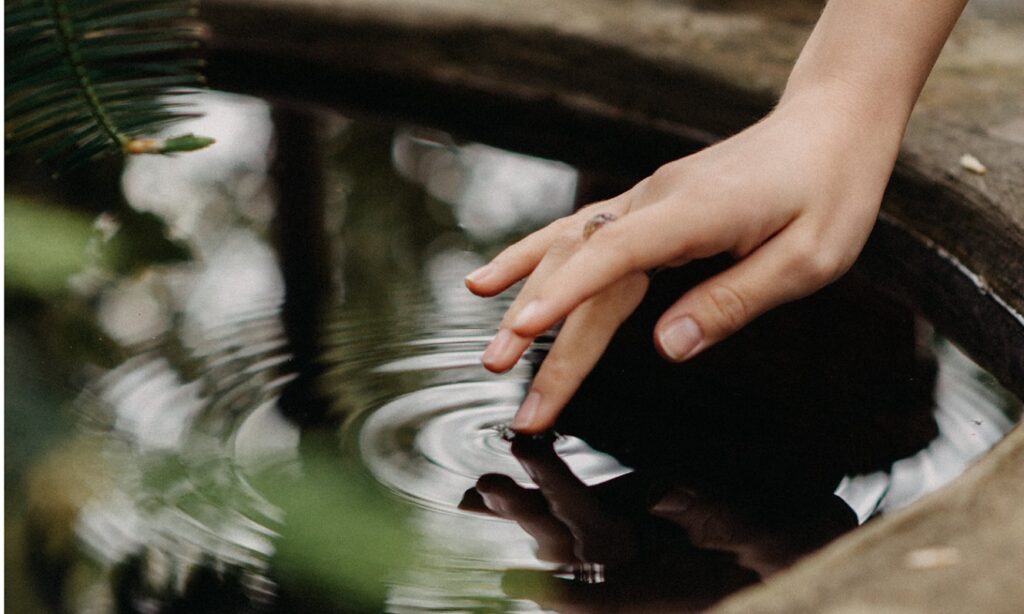 A person dipping their finger onto water surface. 