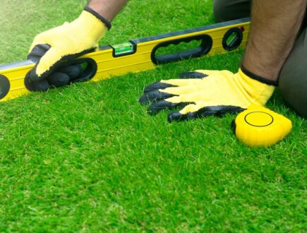 A man on his knees levelling a lawn with a spirit level
