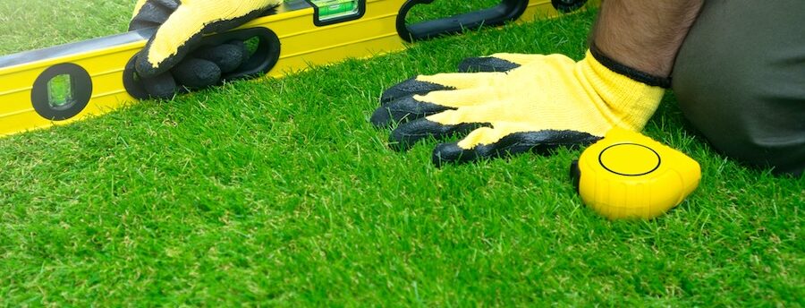 A man on his knees levelling a lawn with a spirit level