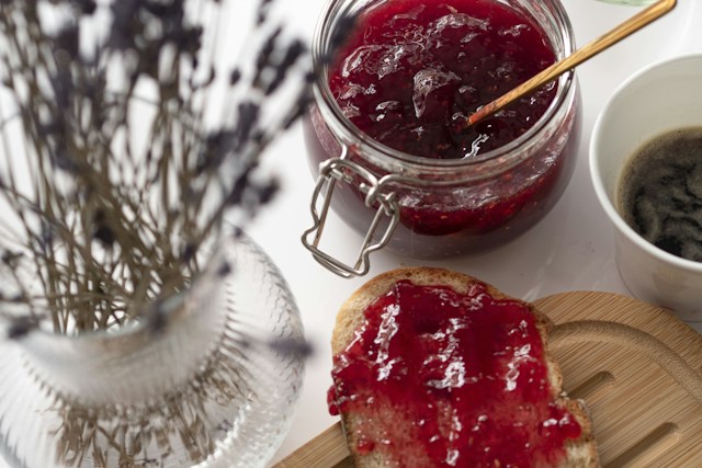 A jar of raspberry jam and some jam spread on toast